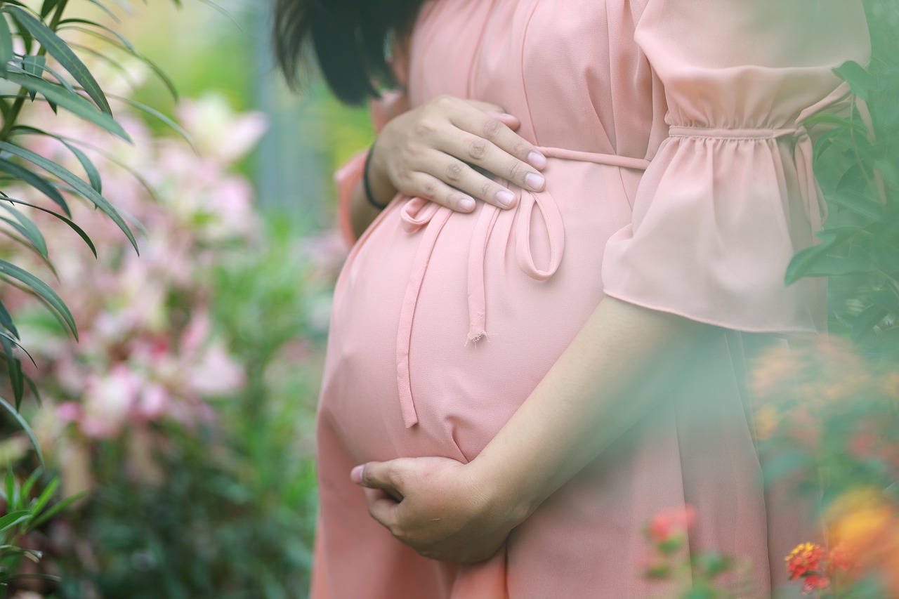 Pregnant woman in a pink dress in a garden among plants