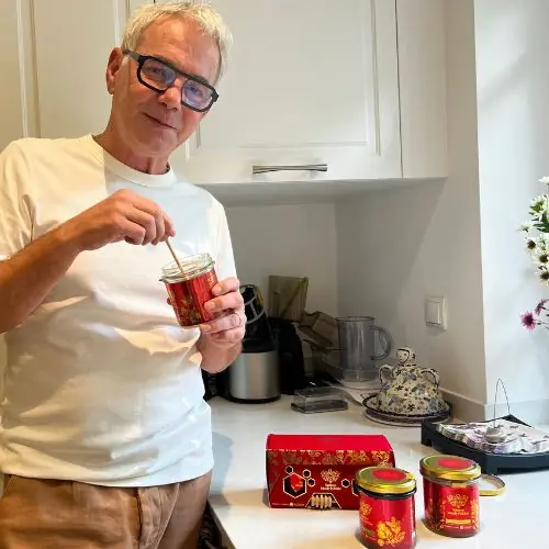 Een man schept Yerbador Rauwe Acaciahoning met een lepel uit een pot naast een rode cadeaudoos