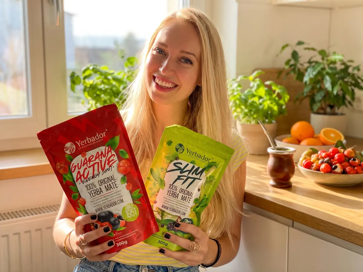 Smiling blonde woman in a sunny kitchen holding Guarana Active and Slim Fit packs
